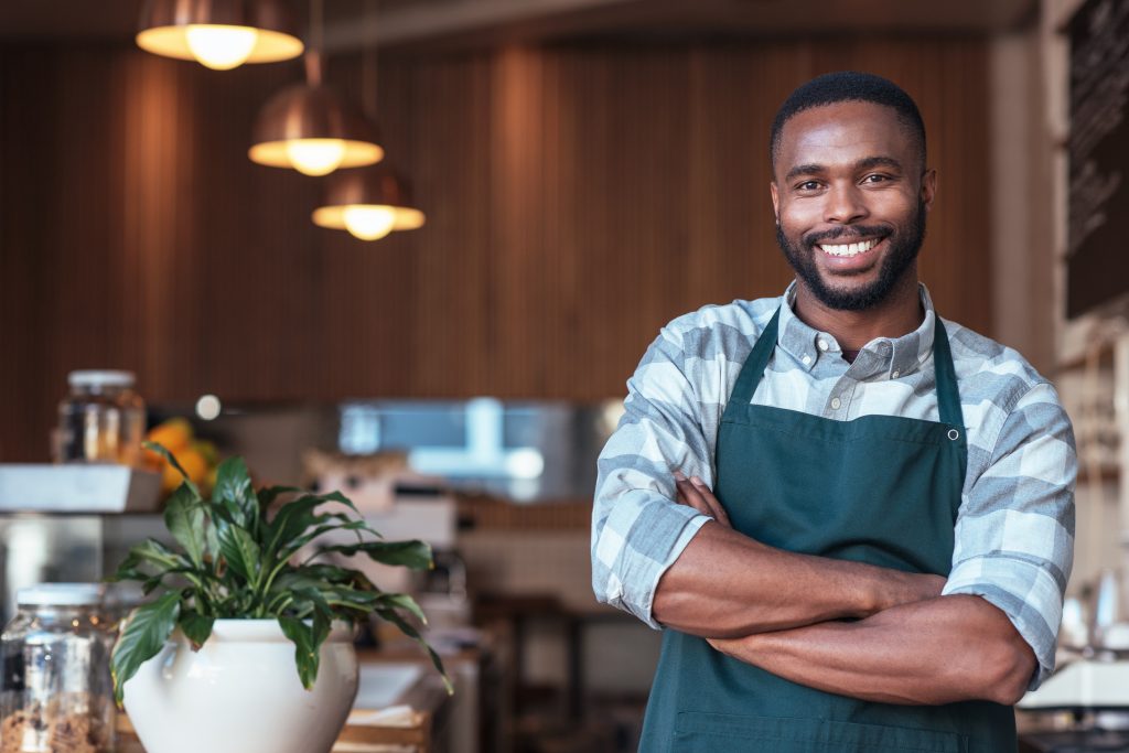 Smiling African entrepreneur standing at the counter of his cafe